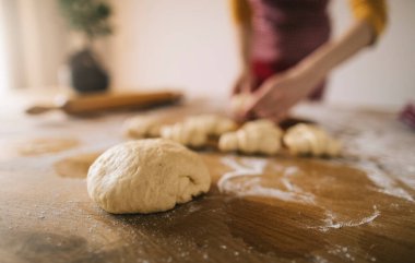 Ev yapımı ekmek. Mutfak masasında seçici hamur odağı ve arka planda önlük takan kadın silueti