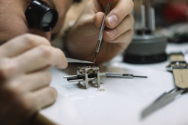 Saatçi kol saatini, mekanik saati tamir ediyor.