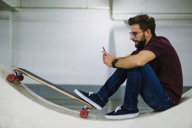 Genç sakallı hippi akıllı telefon kullanıyor.