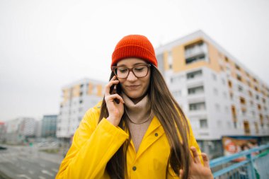 Sarı yağmurluklu genç kadın akıllı telefon kullanıyor.