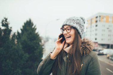 Akıllı telefondan konuşan genç bir kadın. Gülümseyen milenyum kızı dışarıda cep telefonuyla konuşuyor..