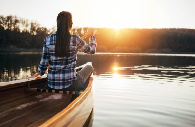 Gün batımında kanoda kürek çeken kadının arka görüntüsü. 