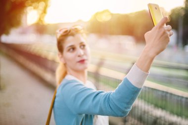 Gün batımında parkta kendi portresini yapan güzel bir kız. Genç bir kadın selfie çekiyor.