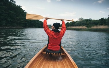 Kırmızı ceketli kanocu arka tarafta kürek çekiyor. Bulutlu bir günde kürek çeken bir adam