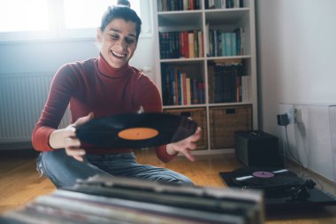 Hippi kızın elinde en sevdiği plak plağı var. Düşük açılı bir kız evde müzik dinlemekten hoşlanıyor.