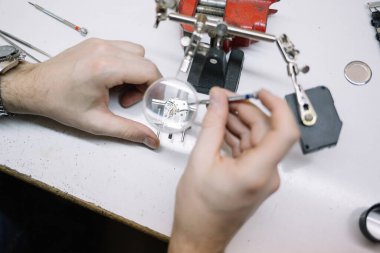 Saatçi kol saatini, mekanik saati tamir ediyor.