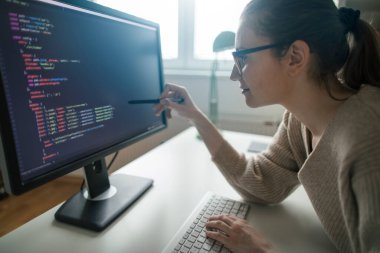 Masaüstü bilgisayarında bilgisayar kodları okuyan genç bir programcı. Bilgisayar kodlarına bakan kadın programcı