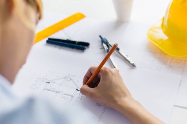Kadın mimar bir plan çizer, tasarım, geometrik şekiller ofis masasındaki büyük kağıt üzerine kurşun kalemle çizer..
