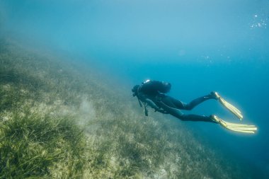 Kayalık zemini olan bir adam suyun altına dalıyor.