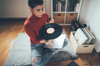 Hippi kızın elinde en sevdiği plak plağı var. Düşük açılı bir kız evde müzik dinlemekten hoşlanıyor.