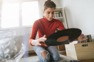 Hippi kızın elinde en sevdiği plak plağı var. Düşük açılı bir kız evde müzik dinlemekten hoşlanıyor.