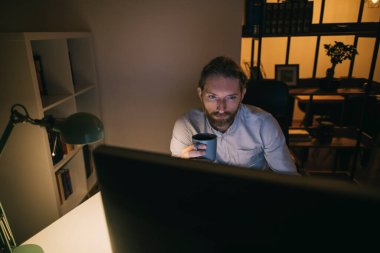 Adam bilgisayarla saatlerce çalışıyor. Evinden çalışan sakallı bir adam.