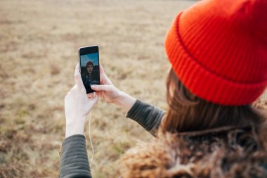 Hippi kız dışarıda akıllı telefon kullanıyor. Kadın selfie çekiyor.