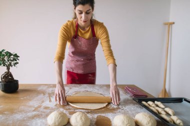 Ekmek hamurunu mutfak masasında oklavayla yoğuran kadın. Ev yapımı pişirme.