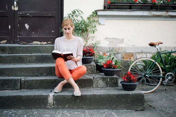 Merdivenlerde kitap okuyan genç bir kadın.