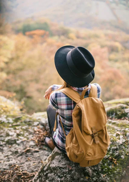 Uçurumda oturan şapkalı bir kız.