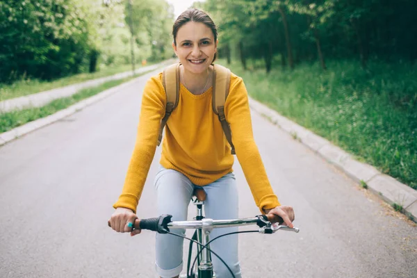 Sarı kazaklı hoş bir kadın parkta bisiklet sürüyor.