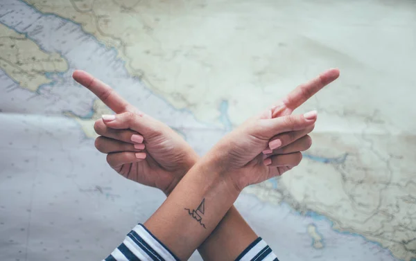 İşaret parmaklarıyla çapraz eller zıt yönleri gösterir. Ayak bileğinde küçük bir gemi / yelkenli dövmesi var. Seyahat, turizm, macera konsepti