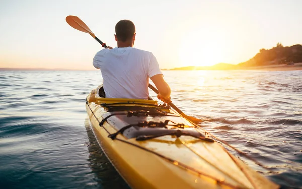 Man kayaking on lush sea water on sunrise, summer time