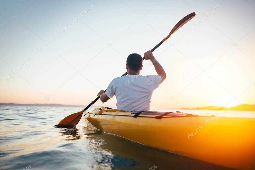 Man kayaking on lush sea water on sunrise, summer time 