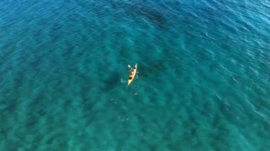 Kanocu adamın denizde kürek çekerken yüksek açılı görüntüsü. Turkuaz denizdeki sarı kanonun havadan görünüşü