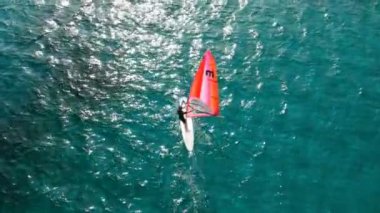 Rüzgâr sörfü tahtasında turkuaz denizde süzülen adamın hava görüntüsü. Rüzgarı yakalayan rüzgar sörfçüsünün görüntüsü.  