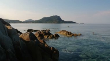 Turkuaz deniz suyuyla kayalık resiflerin üzerinde ilerliyorlar.