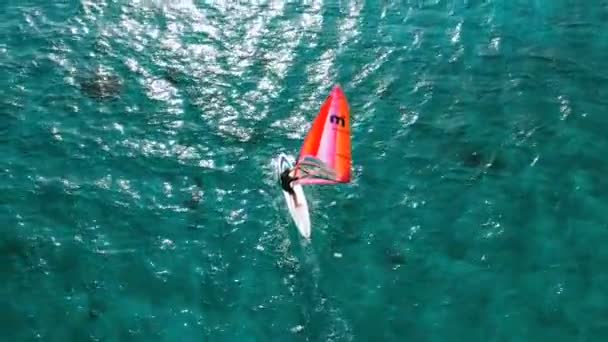 ターコイズブルーの海を横切るウィンドサーフィンボード上の人間の空中ビュー 風をキャッチするウィンドサーファーの追跡ショット — ストック動画