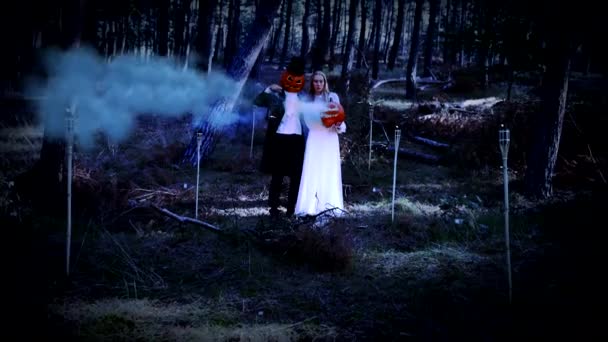 Chica rubia y un hombre de cabeza de calabaza de pie en el bosque en la temporada de Halloween — Vídeos de Stock