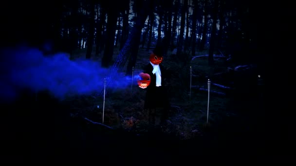 森の中で青い煙と巨大なカボチャを保持している不気味なカボチャの頭の男 — ストック動画