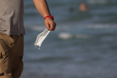 Elinde maskeyle yürüyen kişi