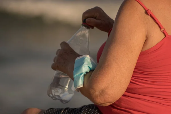 woman from behind sitting on a rock on the beach with the mask on her forearm