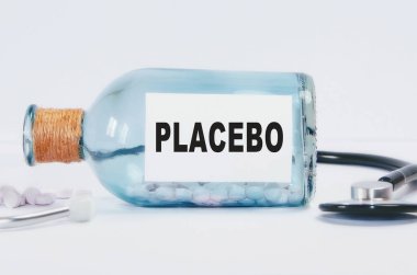 İçinde haplar ve steteskop olan cam bir şişenin üzerindeki PLACEBO kelimesi..