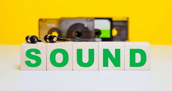 黄色の背景に木製のキューブにサウンド碑文 オーディオカセットやヘッドフォン 音楽の概念 — ストック写真
