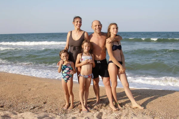 Retrato de grupo de una familia sana de 5 personas, mamá, papá y tres hijas en una playa soleada están de pie en la arena en trajes de baño, y sonriendo con caras felices Imagen de stock