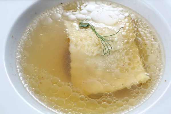 Minimalistic serving of food, white transparent chicken broth in a plate of rice, cheese and dumplings, decorated