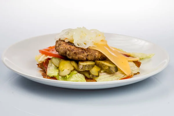 Hamburguesa con chuleta de res, tocino, tomates y rebanadas de queso, sazonada con salsa y ensalada verde para un menú de restaurante sobre un fondo blanco aislado Imagen de archivo