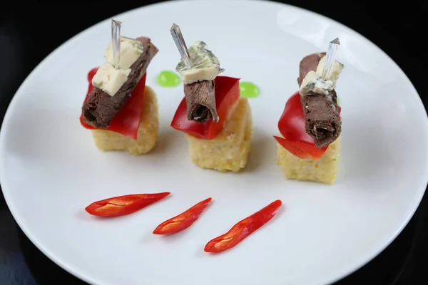 sliced meat, rolled into a roll, canapes with blue cheese and red pepper, on a skewer, close-up