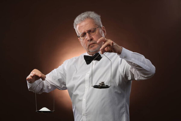 Elderly gray-haired man 50s, in white shirt, glasses and bow tie weighing something on scales with kettlebells