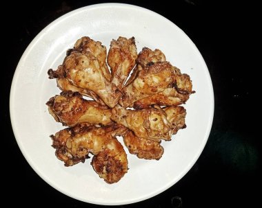 Siyah arka planda bir tabakta fırında tavuk kanadı.