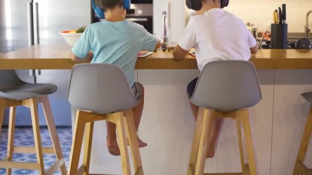 Két Gyerek Hátukon Fülhallgatóval Akik Mobilokat Nézegetnek Tabletjeikkel Játszanak Egy — Stock videók