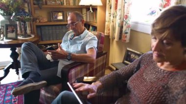 İzleme atışı uzaklaşıyor. Rahat yaşlı çift rahat bir oturma odasında mobil cihazlarına bakıyor. Büyükanne ve büyükbaba yaşam tarzı, gündüz.