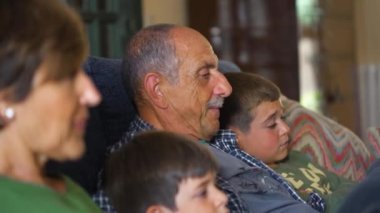 Kanepede oturup televizyon izleyen bir aile. Büyükbabalar ve torunlar film izlemeye yoğunlaşmışlar..