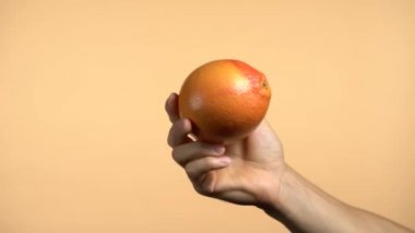 Renkli turuncu arka planda greyfurt gösteren beyaz bir erkek eli. El sağ taraftan geliyor..