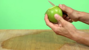 Yeşil bir elma soy. Beyaz eller yeşil bir elmayı küçük bir bıçakla soyarlar. Yeşil stüdyo geçmişi.