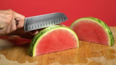 Kırmızı stüdyo arka planında bir karpuz dilimlenmiş bıçakla beyaz eller..