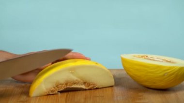 Bıçaklı beyaz eller mavi bir stüdyonun arka planında sarı bir kavundan bir dilim kestiler..