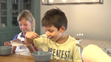 Beyaz çocuk evde mısır gevreği yerken kız kardeşi koruyucu bir maskeyle oynuyor. Kahvaltısını bitirir ve annem okuldan önce koruyucu maskesini takar. Okulun ilk günü. Okula dönüş Coronavirüs, COVID-19. 