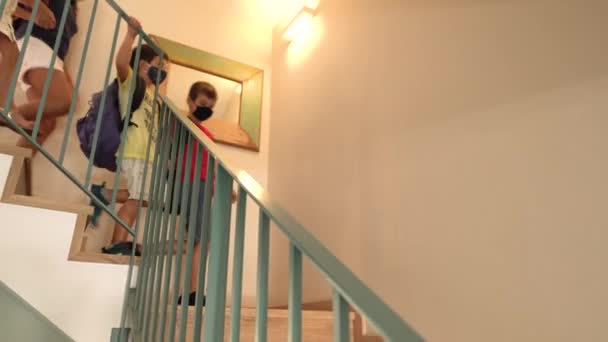 大規模な白人家庭の4人の子供が学校の初日の朝に家から階段を降りてきます 彼らは保護マスクとバックパックを着用 コロナウイルスのパンデミックの間学校に戻る Covid 19の新ルールをコンセプトに — ストック動画