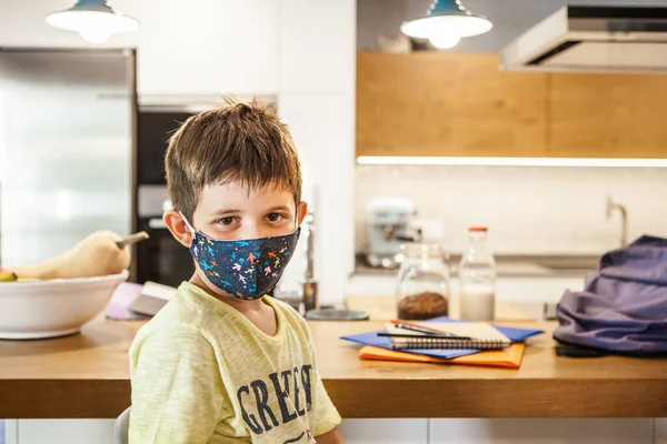 6-years-old caucasian boy with colored protective mask looking at camera. Preschool Kid in modern house kitchen. Daytime, first day of school after coronavirus pandemic. New rules Covid-19.